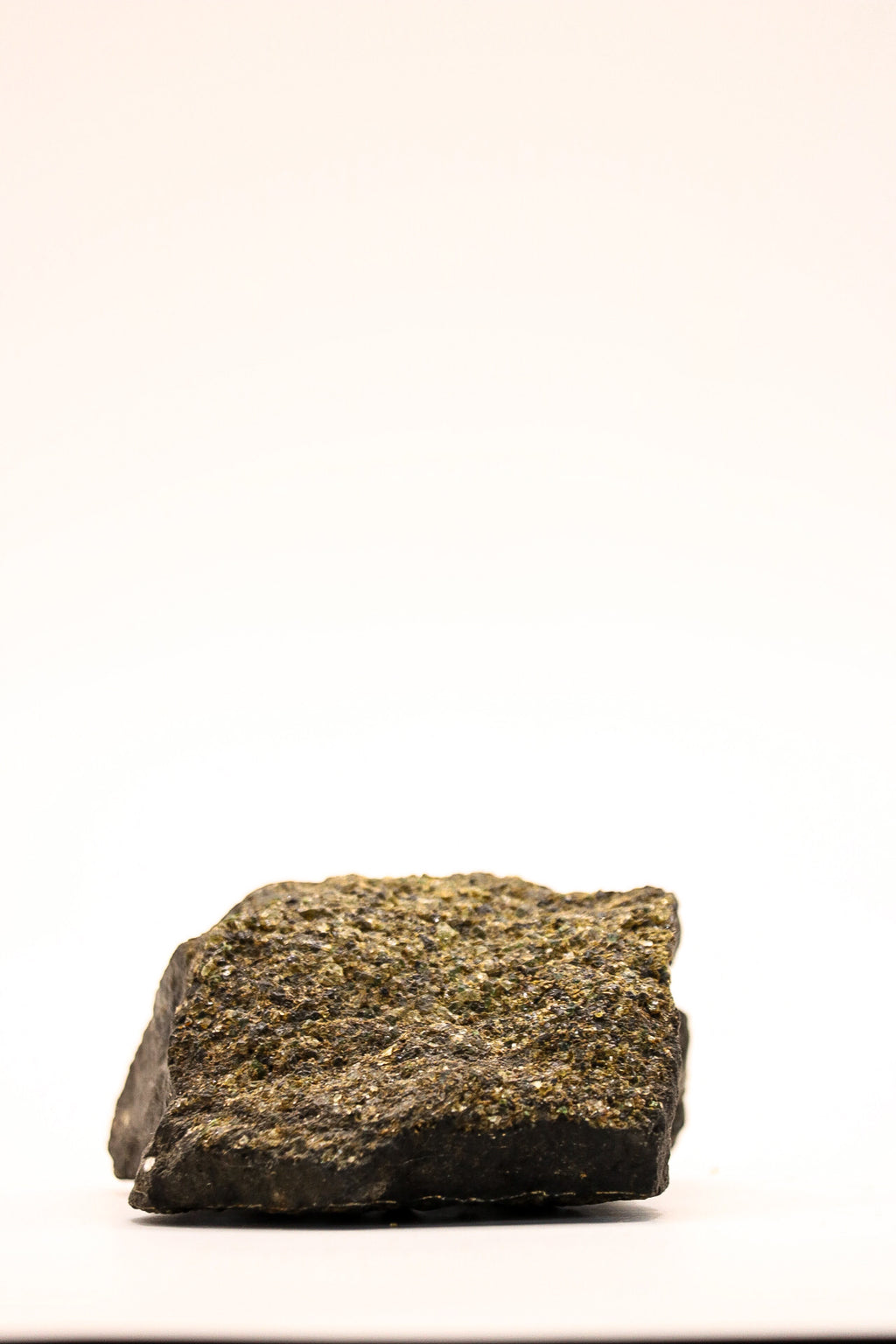 Bovenaanzicht van een ruw peridoot specimen met kleine groene kristallen en donkere matrix