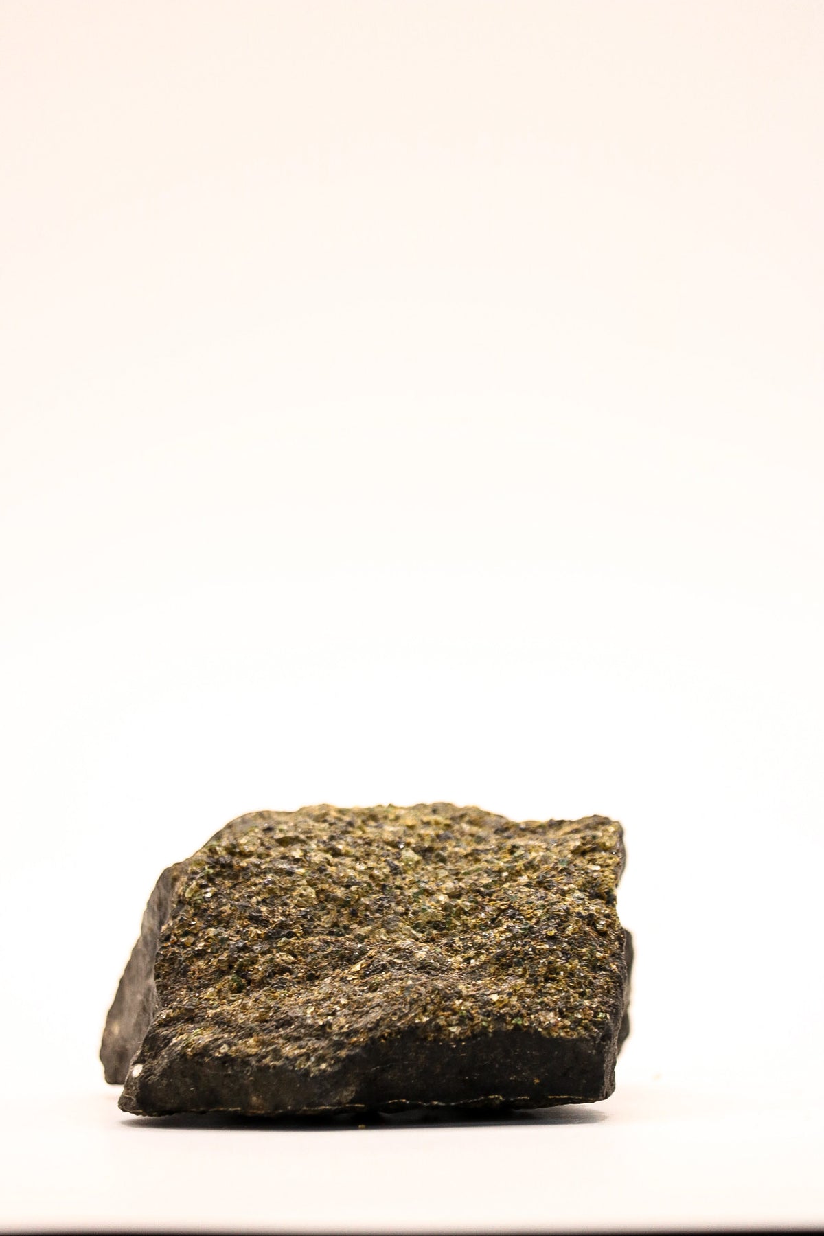 Bovenaanzicht van een ruw peridoot specimen met kleine groene kristallen en donkere matrix