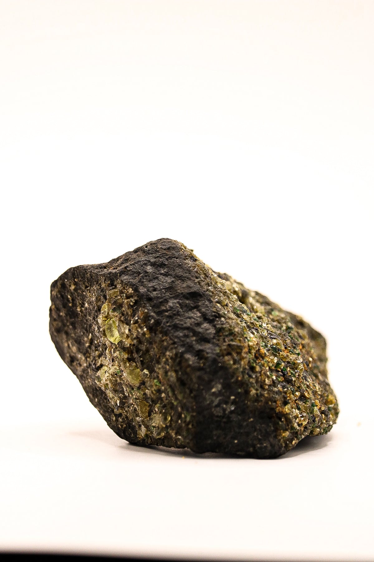 Zijaanzicht van een ruw peridoot specimen met donkere natuurlijke matrix